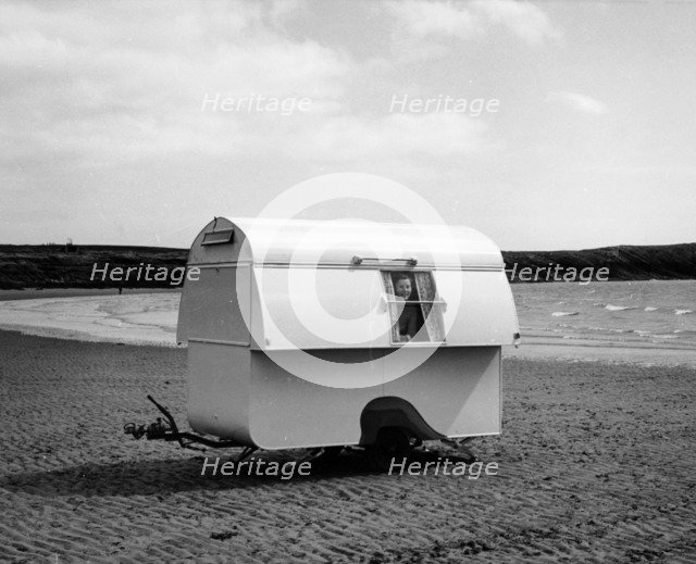 Woman smiling from the window of a trailer caravan on a beach, (c1960s?). Artist: Unknown