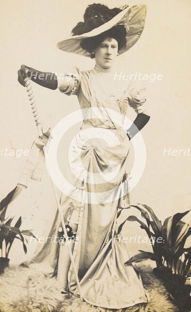 An man in drag is wearing a revealing dress and holding a staff, posing with his..., 1909. Creator: Unknown.