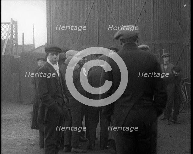 Male Civilian in a Flat Cap Facing a Wall. Another Male Civilian Carries a Sack Over His..., 1924. Creator: British Pathe Ltd.