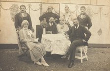 German soldiers, some in drag, pose round a table at a concert party, (between 1910 and 1919?). Creator: Unknown.