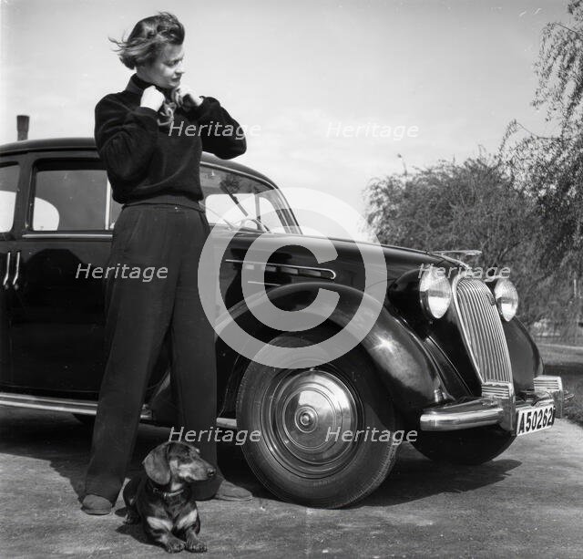 Photographer Kerstin Bernhard stands next to a car with her dachshund, 1955-1960. Creator: Unknown.