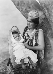 Hupa mother, three-quarter length portrait, seated, facing left, holding baby, c1923. Creator: Edward Sheriff Curtis.