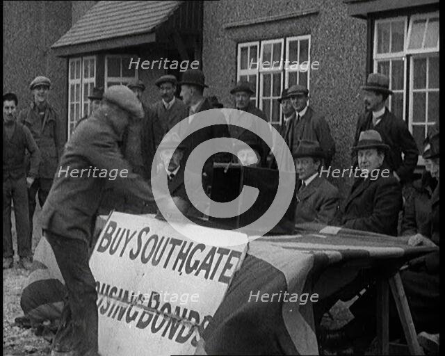 Men Buying Housing Bonds in Southgate. They Take a Piece of Paper from a Box on the Table..., 1921. Creator: British Pathe Ltd.