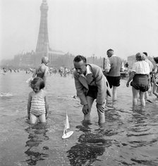 A father and daughter sail a model yacht in the sea, Blackpool, c1946-1955. Artist: John Gay