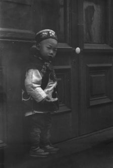 Small boy standing in front of a door, Chinatown, San Francisco, between 1896 and 1906. Creator: Arnold Genthe.