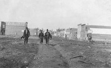 Three men walking down a dirt road, through town, between c1900 and 1916. Creator: Unknown.