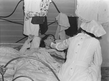 Nurse attending sick migrant woman, FSA camp, Farmersville, Tulare County, California, 1939. Creator: Dorothea Lange.