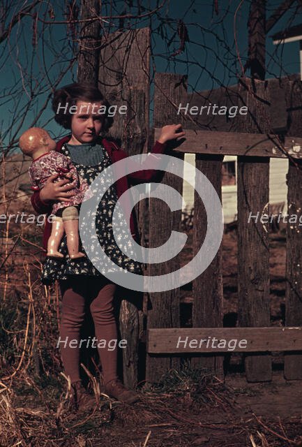 Girl with doll standing by fence, between 1941 and 1942. Creator: Unknown.