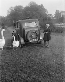 A young girl next to a motor car, probably an Austin 7, with two swans, c1930s. Artist: Unknown.