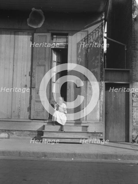 View from across street of a woman sitting on steps, New Orleans, between 1920 and 1926. Creator: Arnold Genthe.