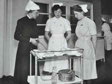 A Sister imparts knowledge and technical expertise to two trainee nurses, c1950s. Creator: Unknown.