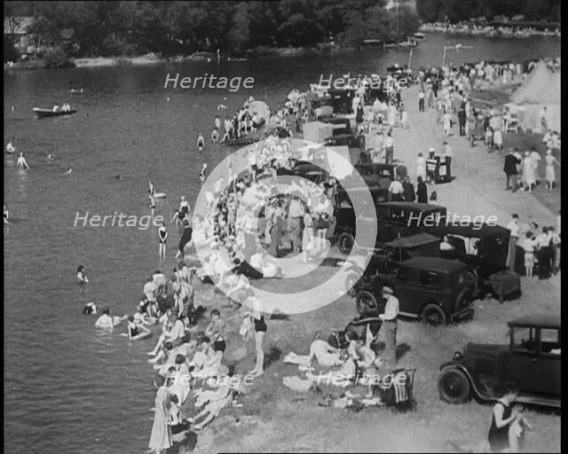 Large Group of People Sitting by a Riverside with Cars, 1933. Creator: British Pathe Ltd.