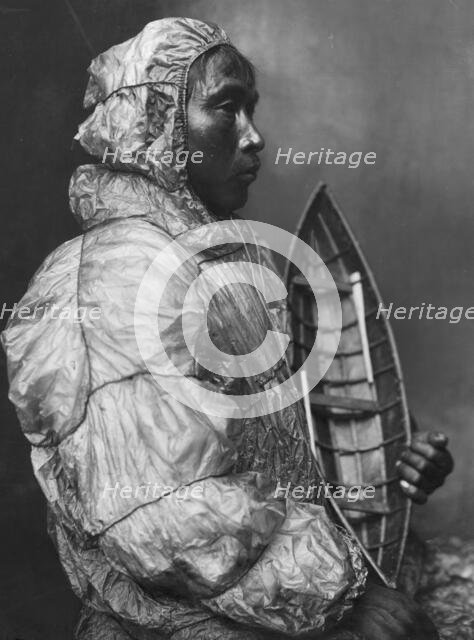 Kayaker wearing water-proof jacket with toy boat he made for his son, between c1900 and c1930. Creator: Lomen Brothers.