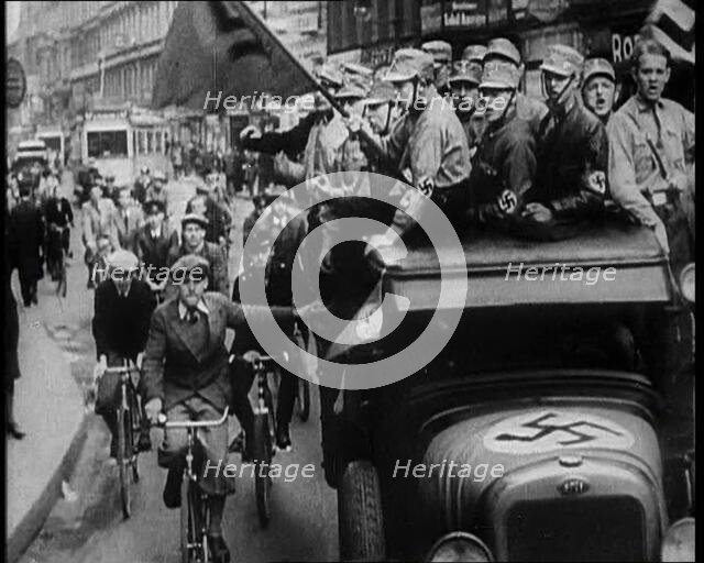 Group of Men in Nazi Uniform Driving Down the Road as Civilians Watch, 1933. Creator: British Pathe Ltd.