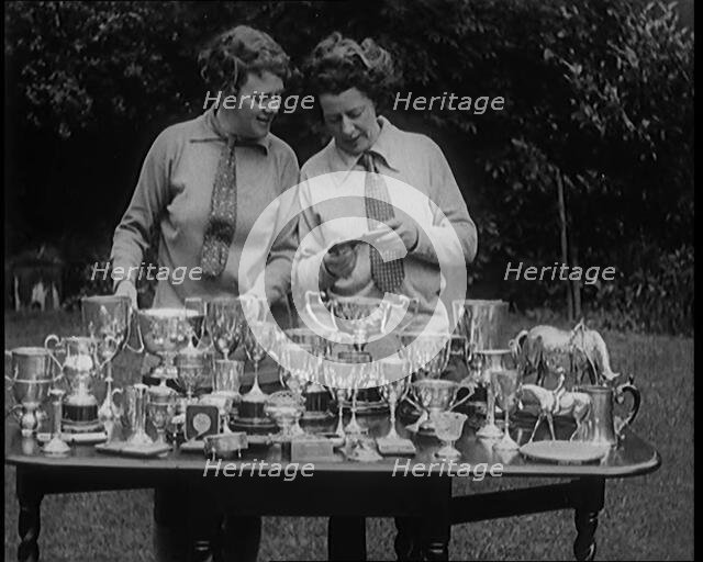 Two Female Civilians Standing Behind a Table Loaded with Trophies, 1920. Creator: British Pathe Ltd.