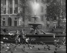 A Boy and a Girl Feeding Pigeons by One of the Fountains in Trafalgar Square with..., 1939. Creator: British Pathe Ltd.