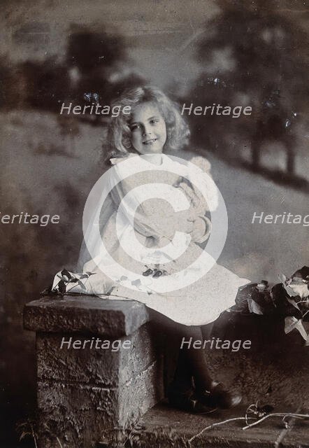 A girl, holding a doll, sitting on a wall, c1890s. Creator: Lock & Whitfield.
