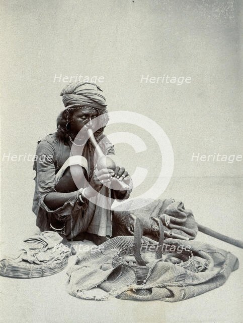 An Indian snake charmer squatting down playing his pipe, with two cobras in a basket in..., c1900. Creator: Unknown.