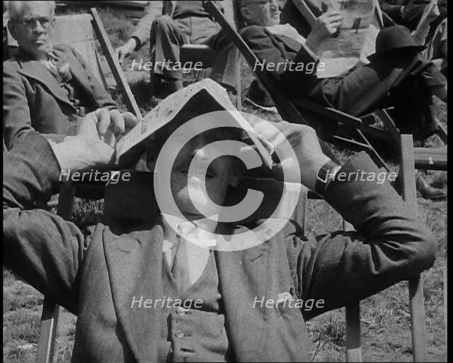 British Man in a Three Piece Suit Sitting in a Deckchair Smiling at the Camera and Holding..., 1938. Creator: British Pathe Ltd.