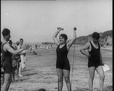 Female Civilian Wearing a Swimsuit Exercising with Elastic Bands on a Beach, 1920. Creator: British Pathe Ltd.