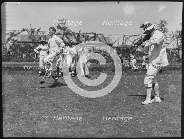 Bampton Morris troupe performing with a fiddler and someone holding a broom aloft, Oxon, 1920-30. Creator: George R Long.