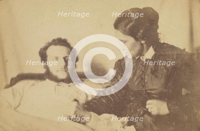 A bearded man lying in bed, his hand held by his wife who is seated next to the bed, 1870-79. Creator: Unknown.