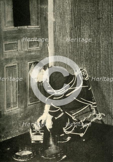 John Nevil Maskelyne performs a 'spirit cabinet illusion', c1910. Creator: Unknown.