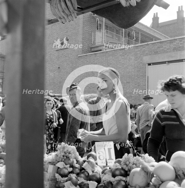 A woman buys fruit at a stall in a North London street market, c1946-c1959. Artist: John Gay