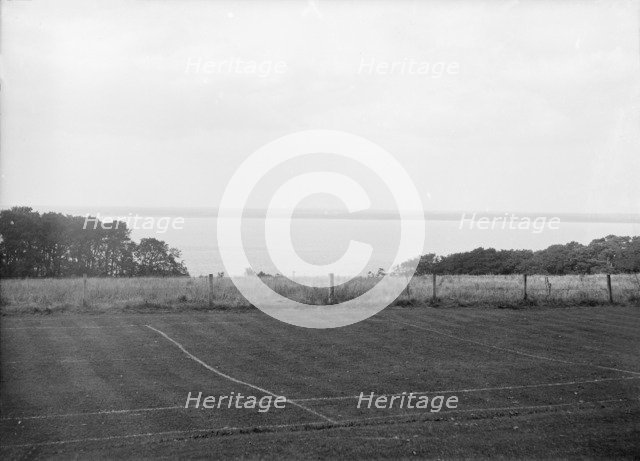 View of a tennis court and the sea, c1935. Creator: Kirk & Sons of Cowes.