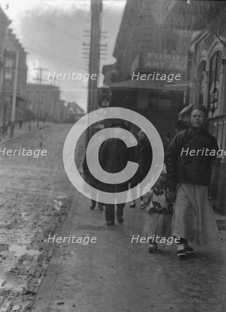 Man and a boy walking down a sidewalk with other people, Chinatown, San Francisco, c1896-1906. Creator: Arnold Genthe.