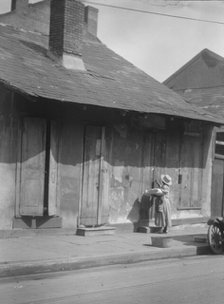 Woman holding a sack standing by the doorway of a building in the French Quarter..., c1920-c1926. Creator: Arnold Genthe.