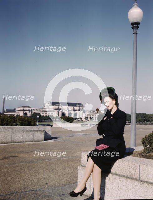 Woman putting on her lipstick in a park with Union Station behind her, Washington, D.C., ca. 1943. Creator: Unknown.