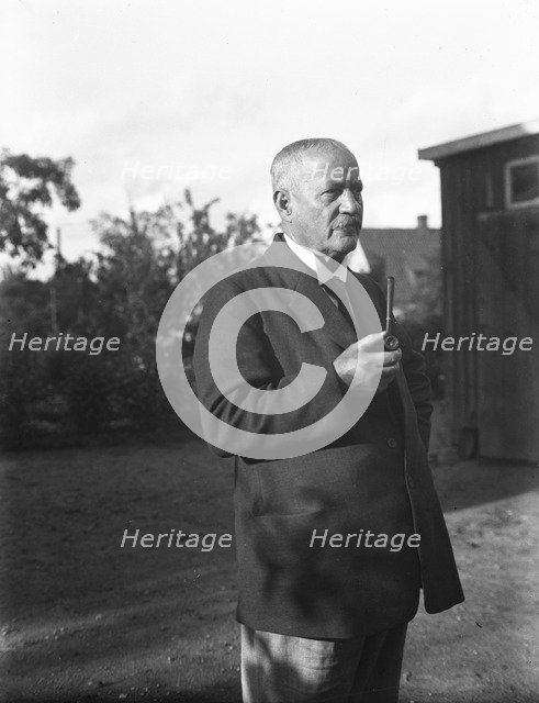 An elderly man with a starched collar, smoking a pipe in his garden, Flyinge, Sweden, 1920s. Artist: Unknown