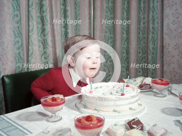Birthday boy blowing out the candles on his cake, c1955.  Creator: Arthur Charles Kirby Ware.