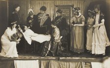 Amateur actors, some in drag, on stage attending to the death of a female character, [1910-1919?]. Creator: Unknown.