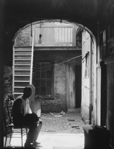 Man seated in archway leading to a courtyard, New Orleans, between 1920 and 1926. Creator: Arnold Genthe.