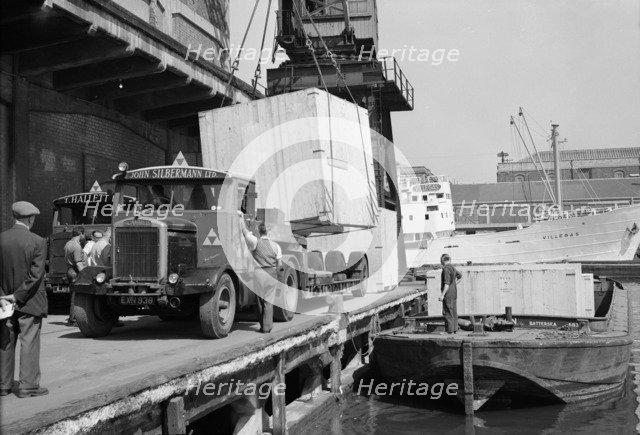 A large crate is hoisted from a lorry onto a barge at the West Quay, Wapping, London, c1945-c1965. Artist: SW Rawlings