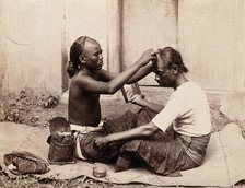 Two Indian men sitting cross-legged; one appears to be a barber..., c1890s. Creator: Unknown.