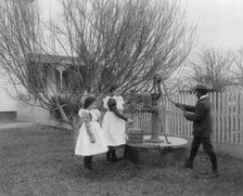 Two girls and a boy pumping water at well of Hampton Institute graduate, 1899 or 1900. Creator: Frances Benjamin Johnston.