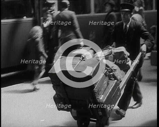 A Male Train Station Porter Pushing a Sack Barrow With Suitcases and Bags on it Along..., 1938. Creator: British Pathe Ltd.