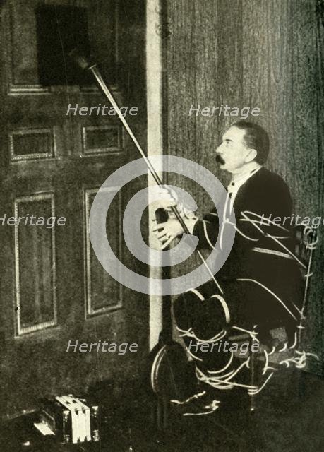 John Nevil Maskelyne performs a 'spirit cabinet illusion', c1910. Creator: Unknown.
