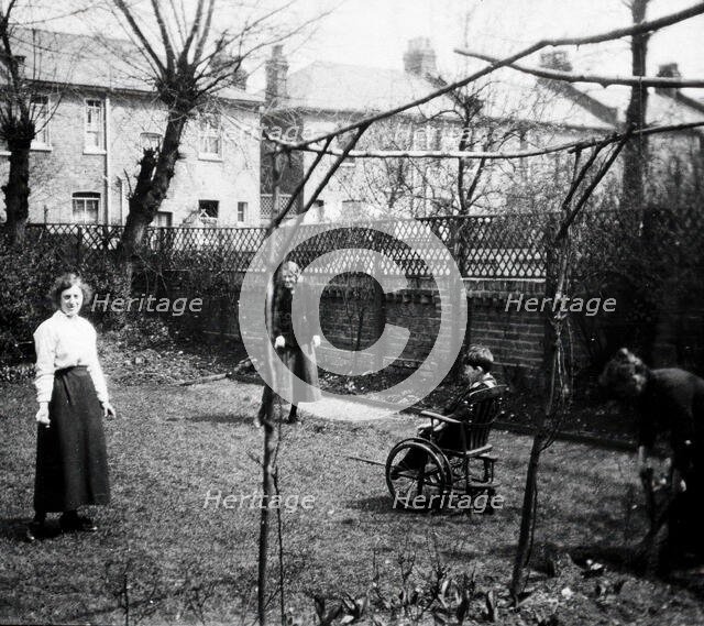 A physically disabled boy sitting in a wheelchair in the back garden of a semi..., c1910/1925. Creator: Unknown.