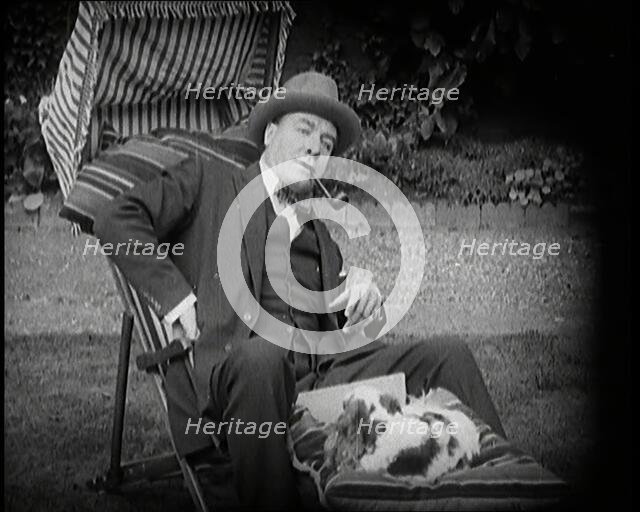 Matheson Lang Relaxing in a Deck Chair Smoking a Pipe With a Dog at His Feet, 1920s. Creator: British Pathe Ltd.