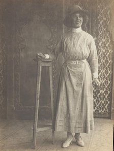 A sailor in drag leans on a high stool, in front of patterned scenery, (between 1910 and 1919?). Creator: Unknown.