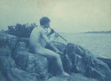 Man posed on rocks, nude, playing pipe (Pan), between 1885 and 1900. Creator: Frances Benjamin Johnston.