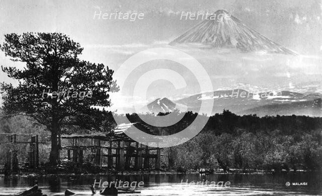 Booths on the river bank against the backdrop of Klyuchevsky volcano, 1922-1923. Creator: Rene Malaise.