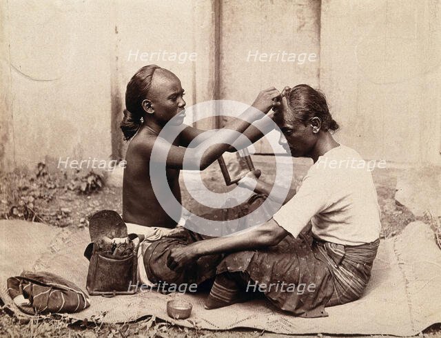 Two Indian men sitting cross-legged; one appears to be a barber..., c1890s. Creator: Unknown.