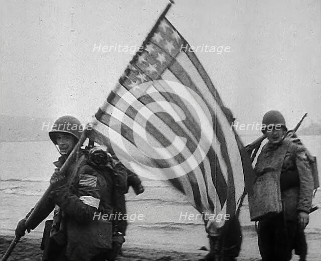 An American Soldier Holding an American Flag on a North African Beach as Part of 'Operation...1942. Creator: British Pathe Ltd.