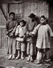 Foochow, China: four people with leprosy, wearing thick clothing, standing outside a wooden..., 1873 Creator: John Thomson.