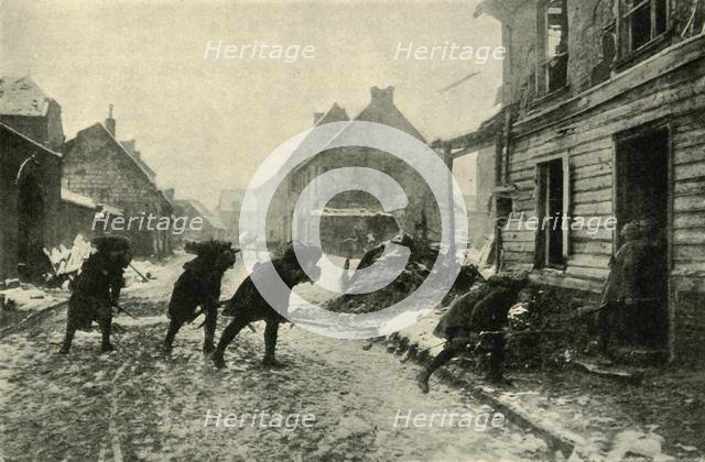 French troops crossing a village street under German fire, First World War, 1914-1915, (c1920). Creator: Unknown.